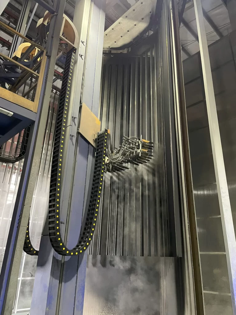 Buồng 2 phun sơn tĩnh điện Gema Thụy Sỹ trong dây chuyền sơn đứng Nhôm Cầu Thịnh, hệ thống súng phun tự động đang phủ sơn lên thanh nhôm.