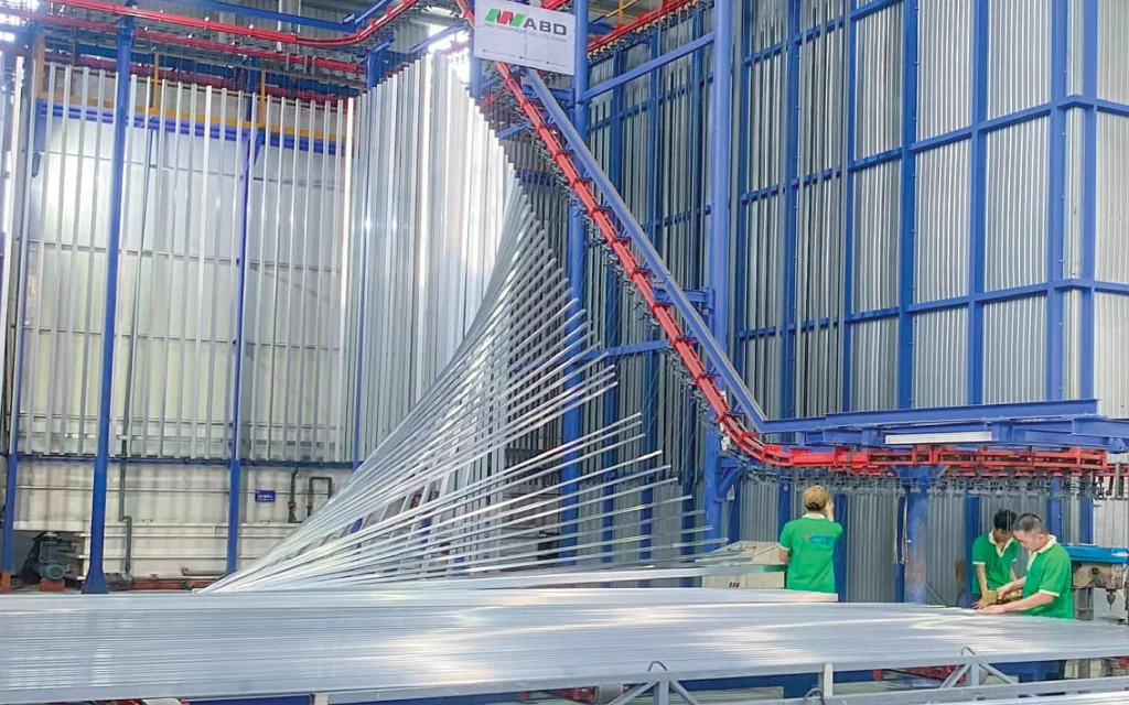 Dây chuyền sơn tĩnh điện dạng đứng tại nhà máy Nhôm Cầu Thịnh với hệ thống treo tự động và công nhân kiểm tra nhôm sau sơn.
